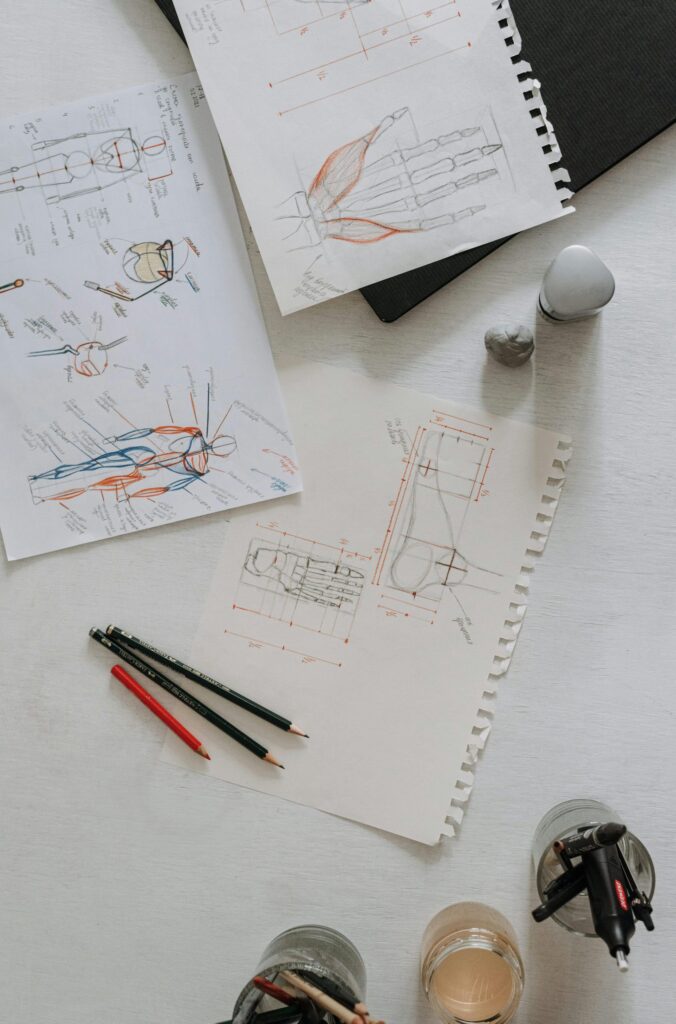 Top view of anatomical sketches with drawing tools on a desk, showcasing artistic process.