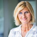Close-up of a smiling blonde woman wearing eyeglasses indoors.
