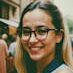 Portrait of a smiling woman with eyeglasses and long hair in an urban setting, captured outdoors.