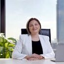 Professional woman smiling at desk with skyscraper view, representing corporate leadership.