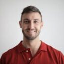 Headshot of a happy man with a beard wearing a red polo shirt against a white background.